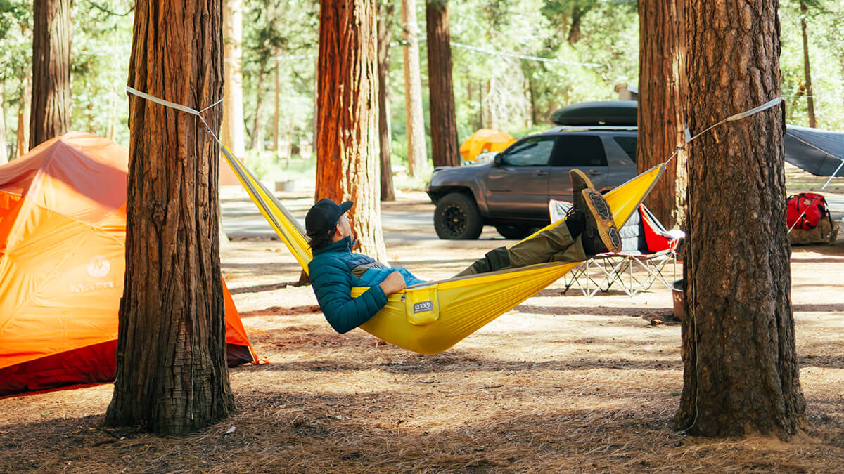 A man lays in his yellow ENO hammock at a campground. 