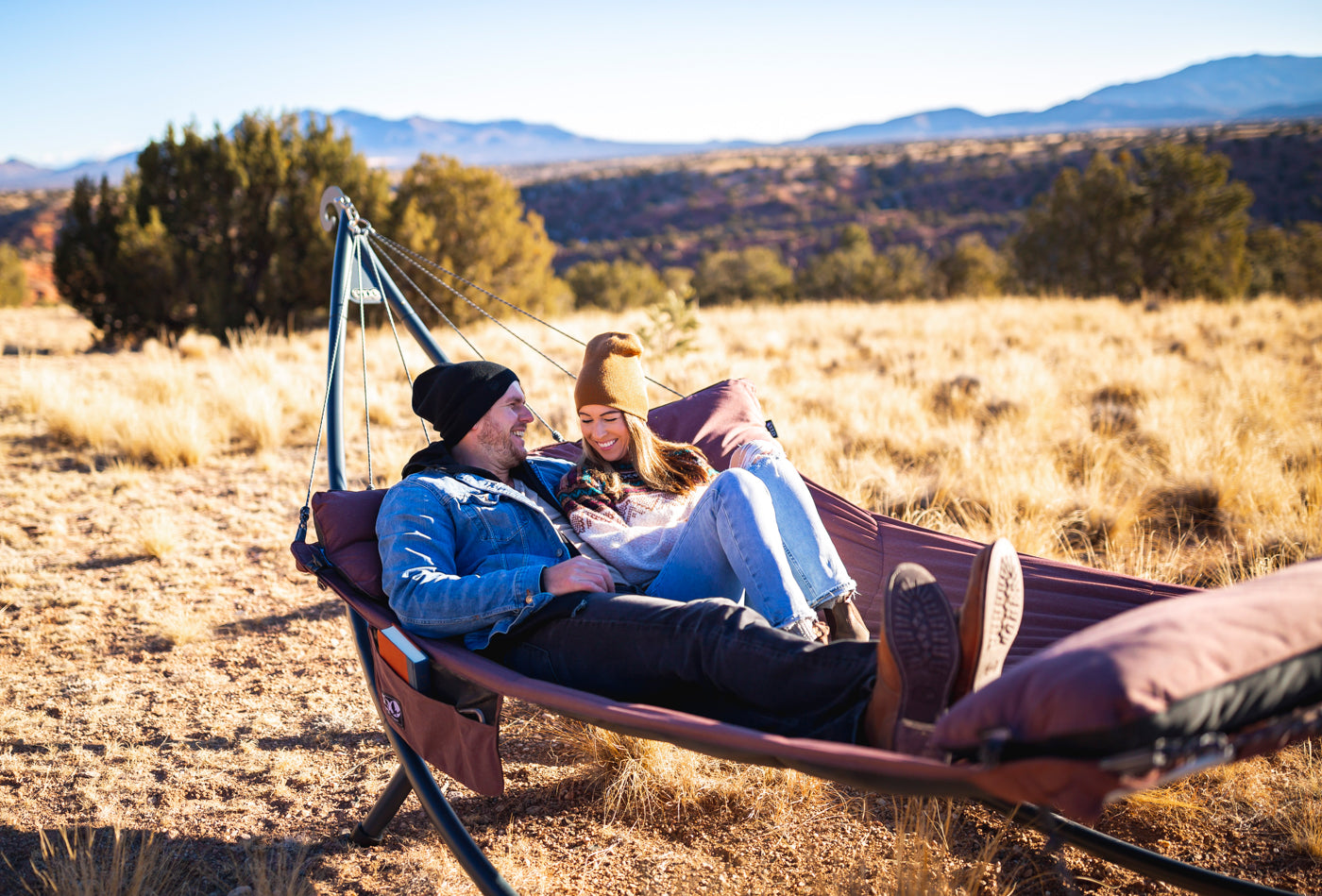A couple in an ENO SuperNest Hammock in a SoloPod XL Hammock Stand in a field