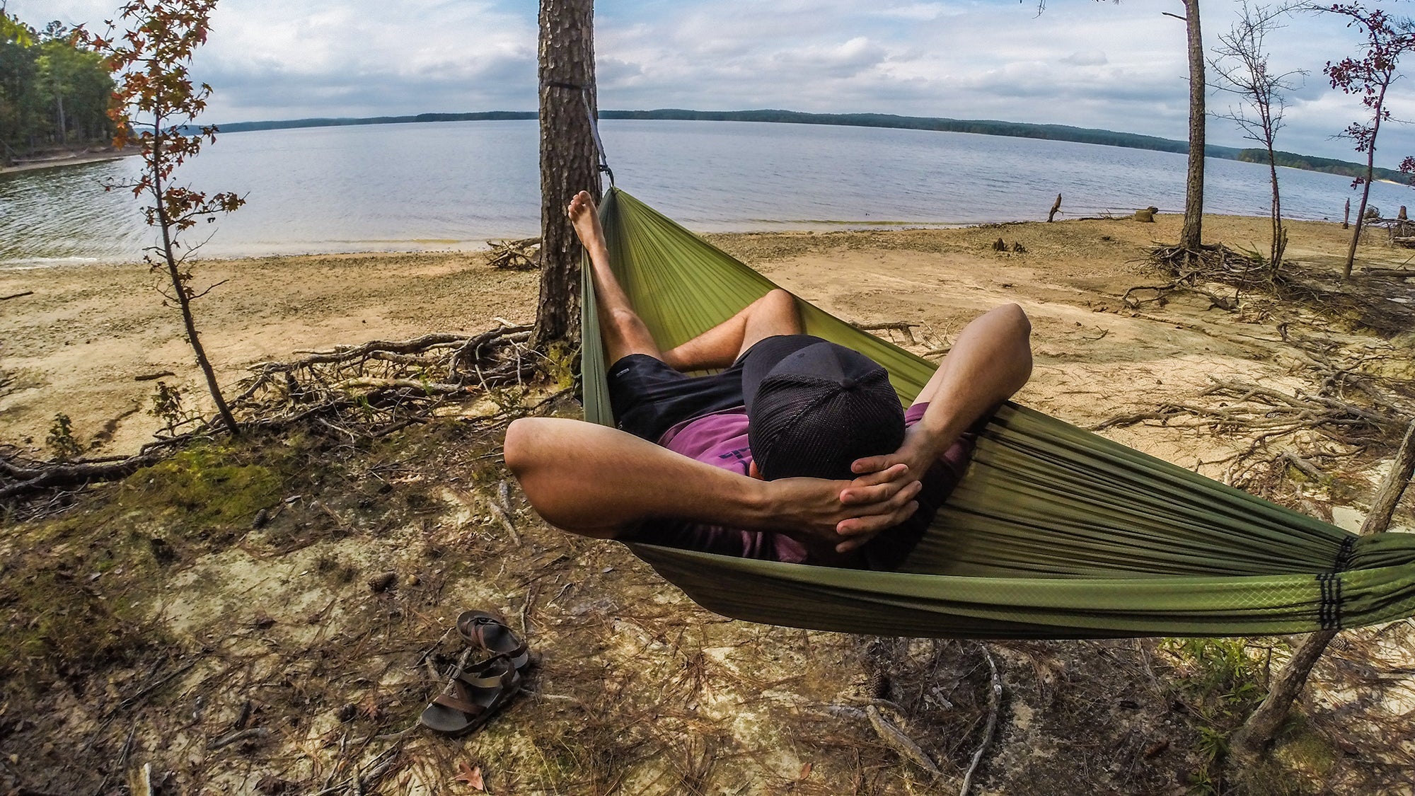A man reclines in an ENO Sub7 Hammock overlooking a lake. 