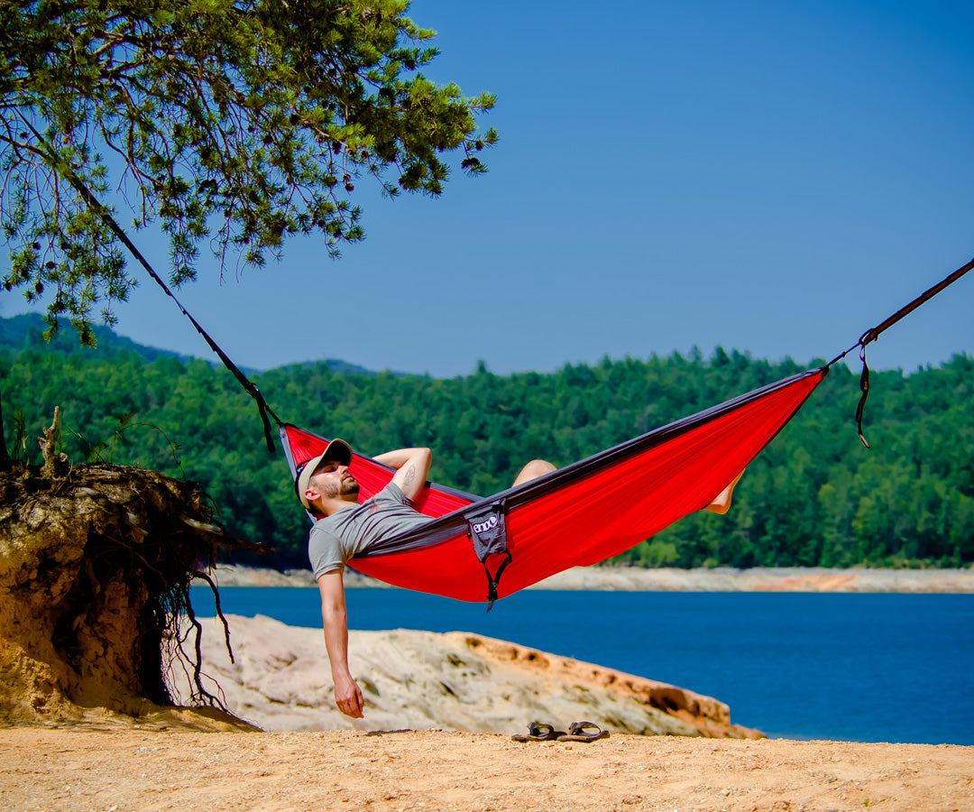 A man relaxing in an ENO hammock with the beach and trees in the background