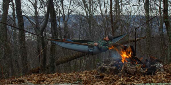 relaxing in hammock in the woods next to a campfire