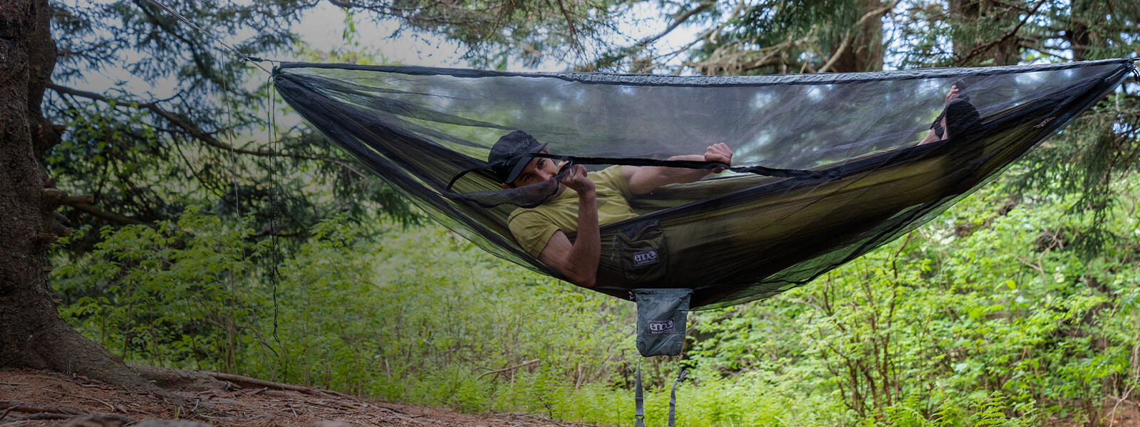 A person zipping up their ENO hammock bug net while hanging in an ultralight hammock.