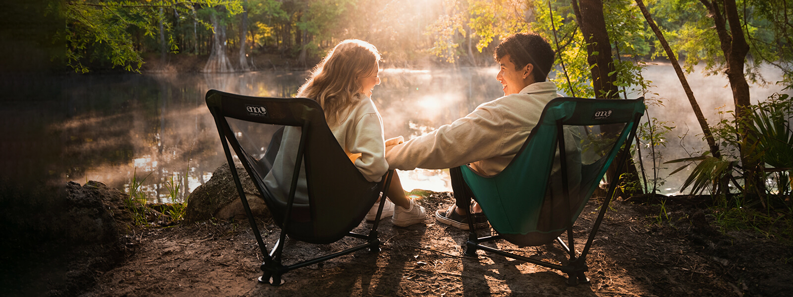 A couple sit beside one another in two ENO camp chairs in front of sunset on pond. 