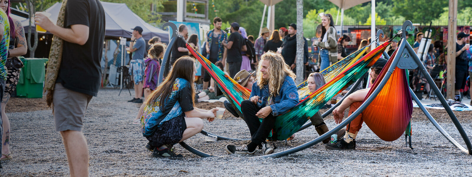 Two people talk while sitting in the ENO ENOpod Triple Hammock Stand at a music festival.