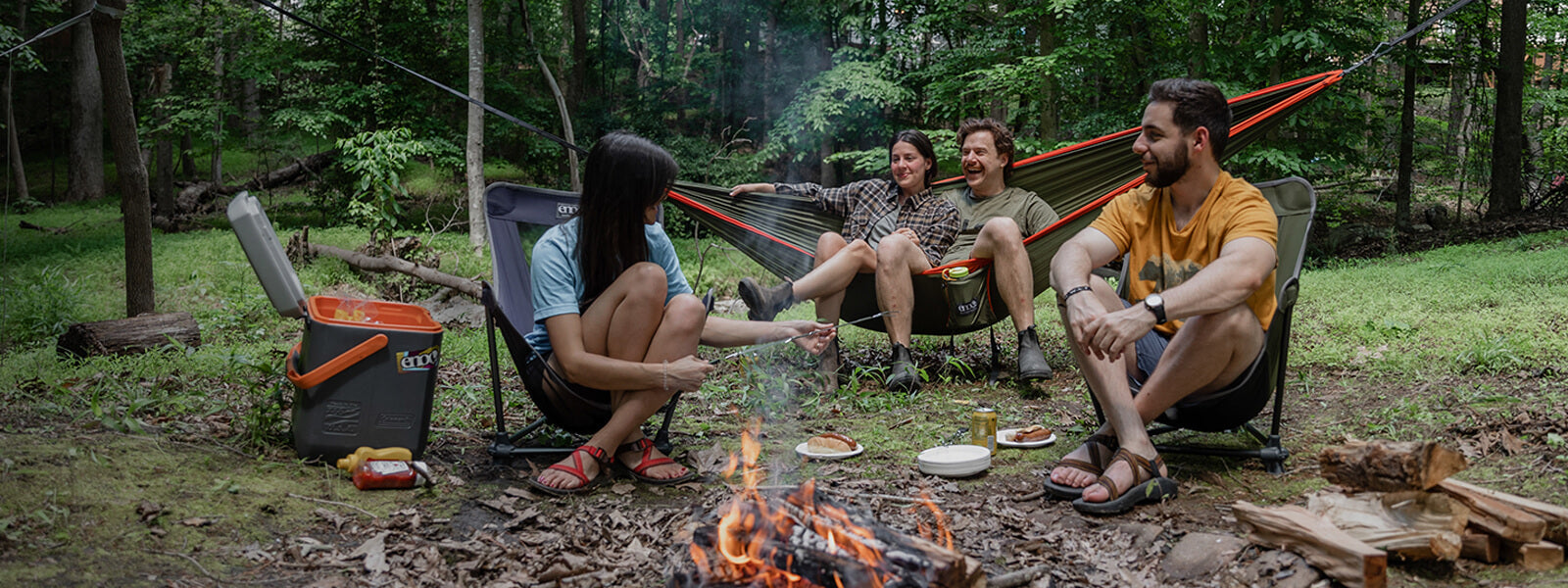 A group of friends sit in front of a fire while sitting in a ENO DoubleNest Hammock and Lounger SL Chairs. 