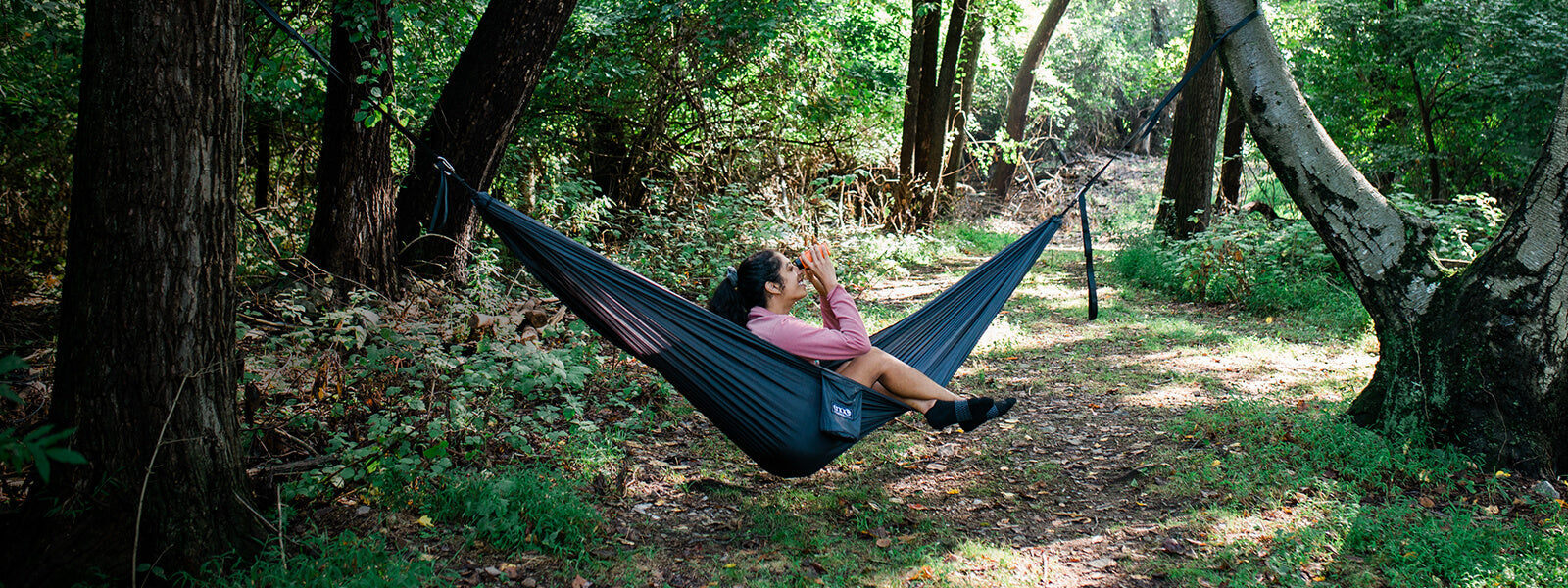 A person sitting up in an ENO portable hammock while looking up through a monocular in a forest. 