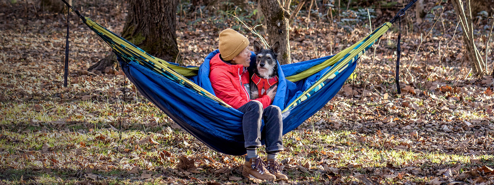 A person and dog sit in an ENO portable hammock wrapped in hammock insulation. 