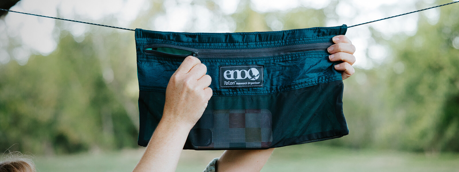 A person unzips the front pocket on an ENO hammock organizer. 