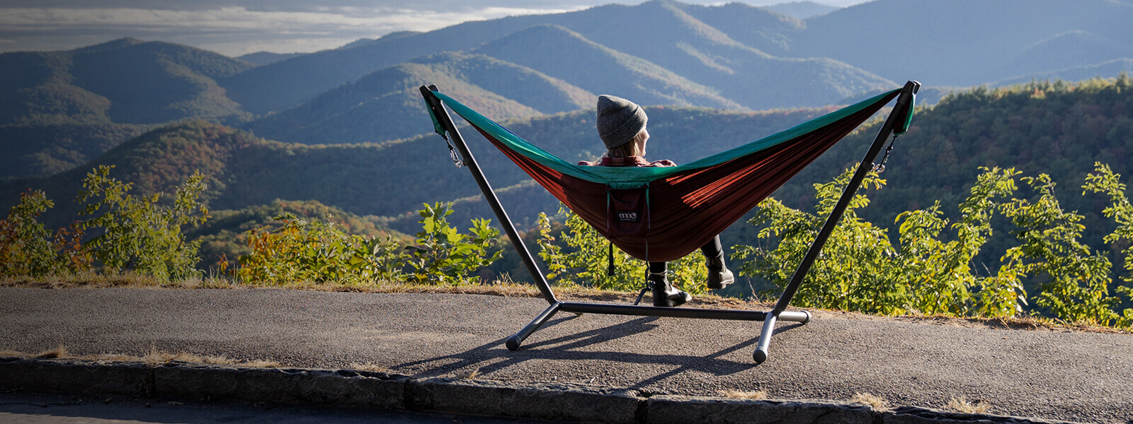 A person sitting in an ENO portable hammock and hammock stand while looking out on mountain overlook.