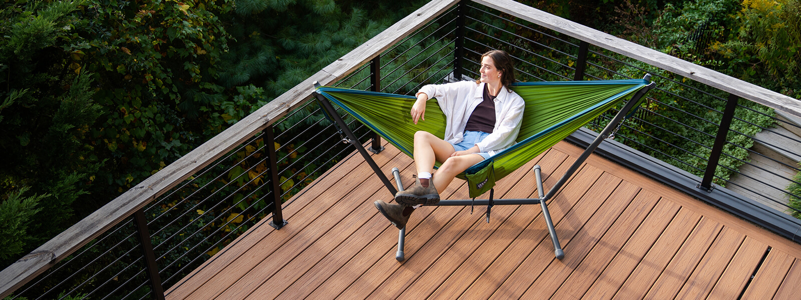 A person sitting on a porch in a ENO portable hammock and portable hammock stand.