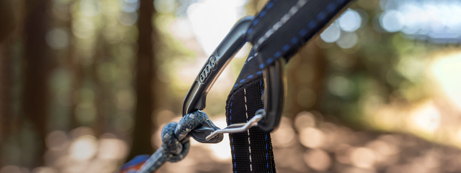 Detail image of an ENO hammock carabiner connected to hammock strap with blurred background.