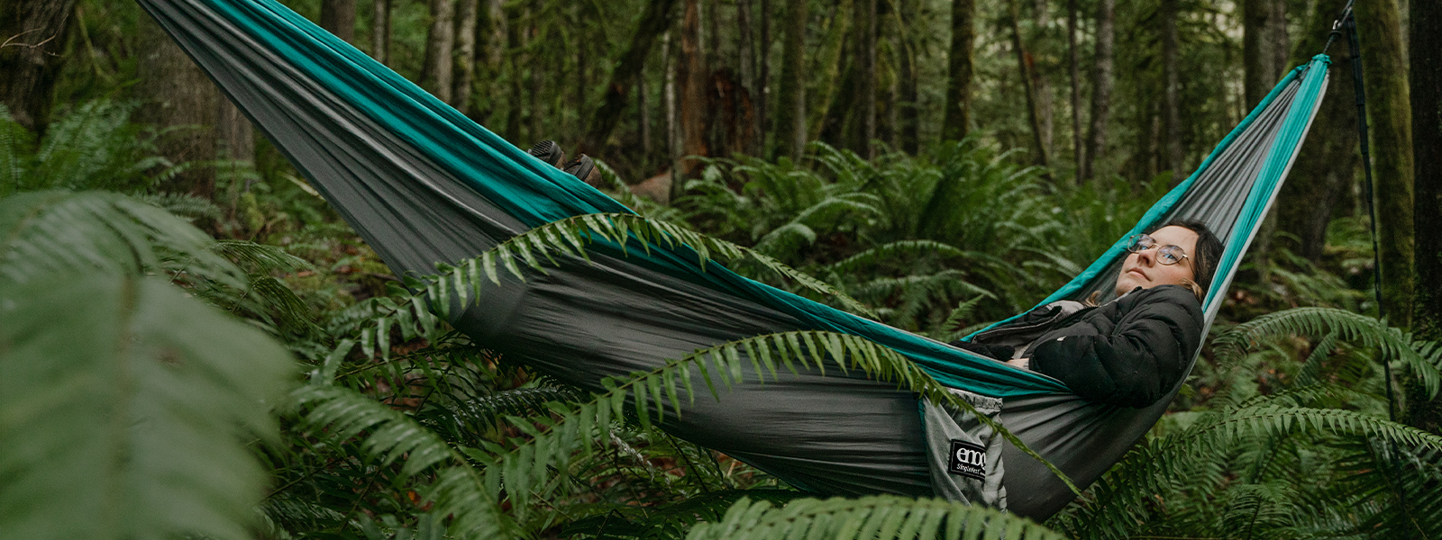 A woman laying back in an ENO portable hammock within a lush north western forest.