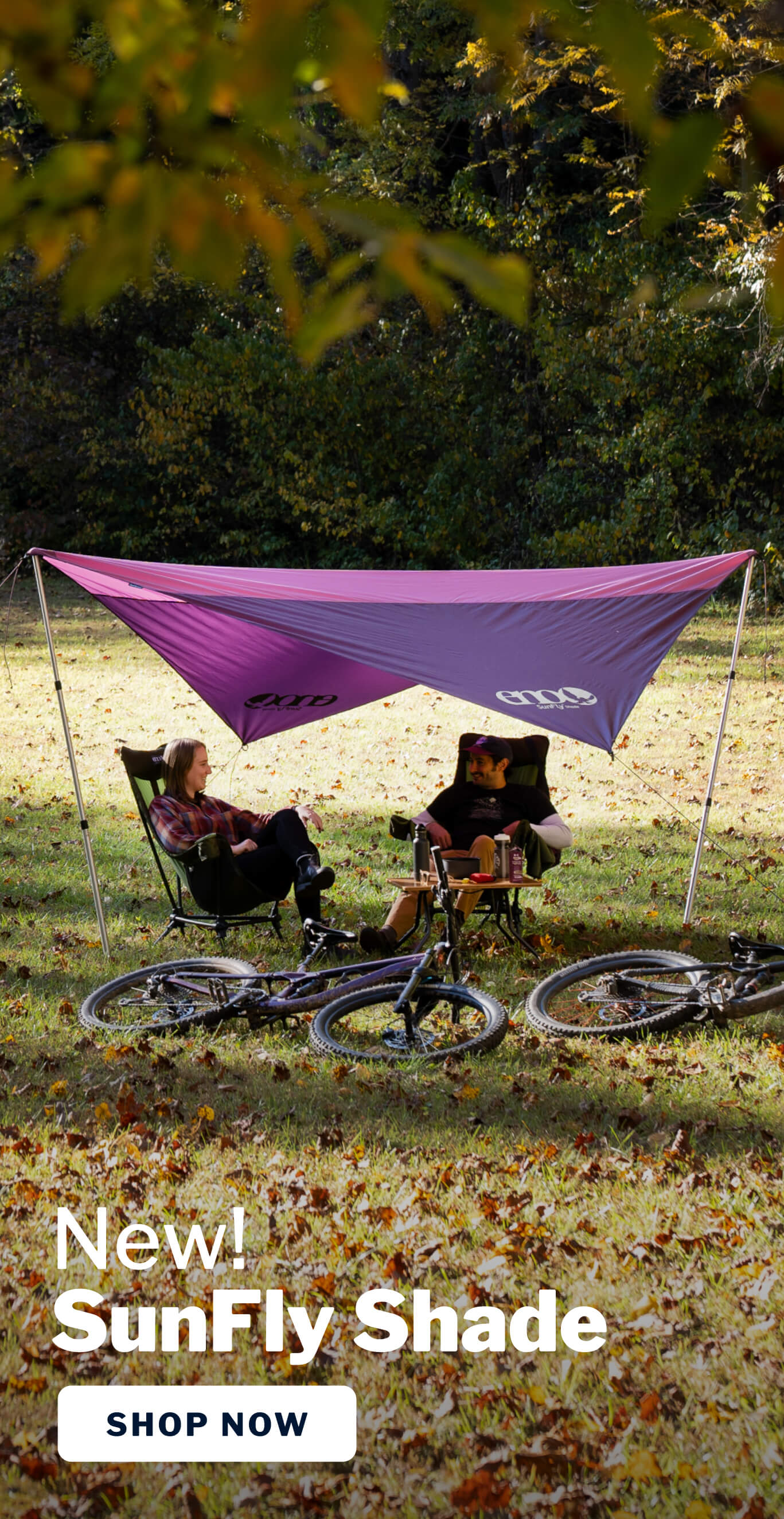 Couple sit shaded under the ENO SunFly Shade in sunny field with bicycles.