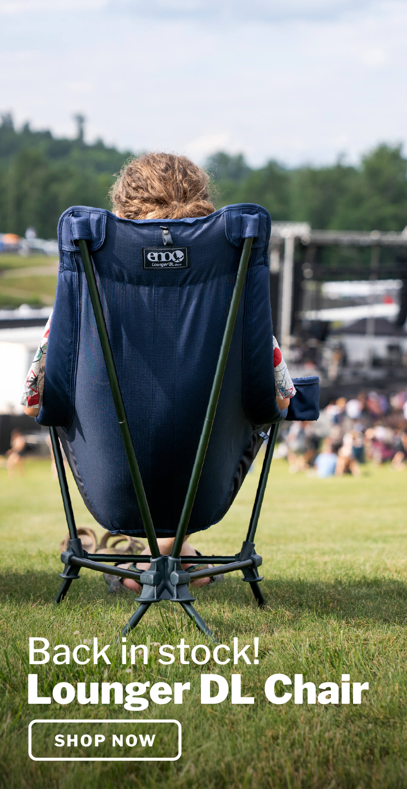 Person sitting in an ENO Lounger DL Chair within a grassy field with soft concert stage and crowd in the background.