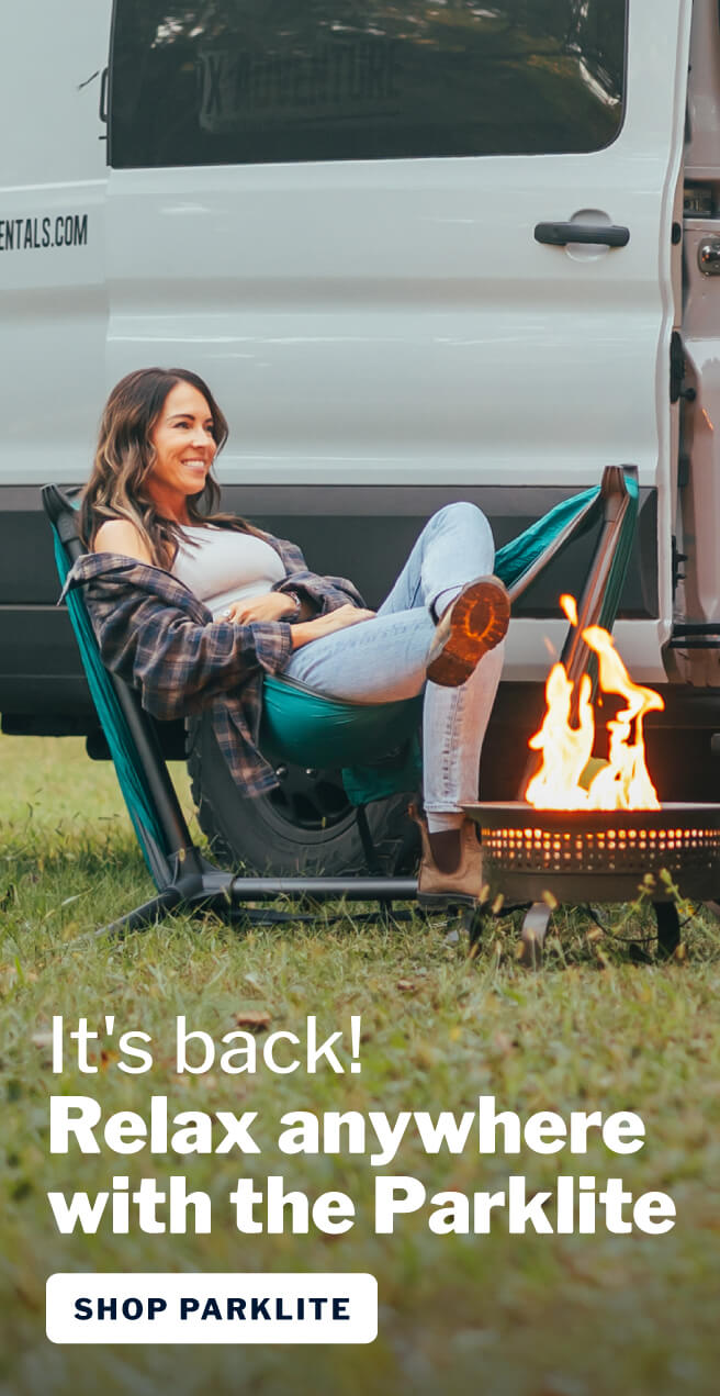 Photo of woman sitting beside fire in front of van while sitting in the ENO Parklite Hammock Chair Stand.