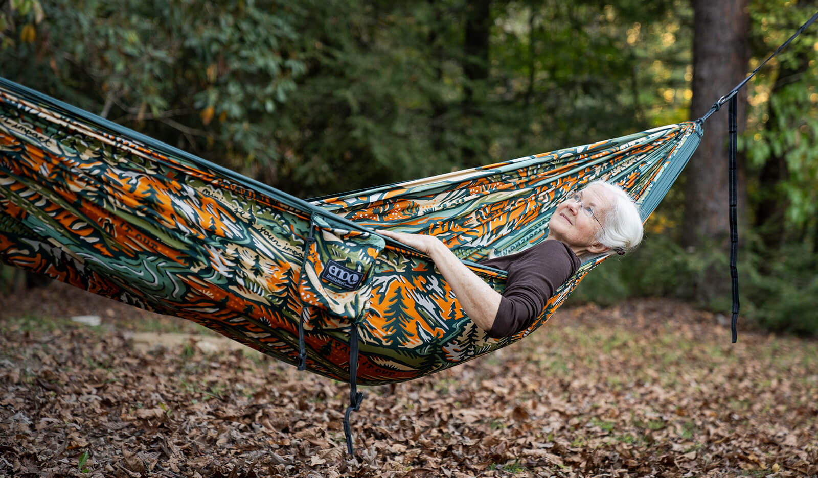 Person relaxing in the colorful American Hiking Society | ENO Giving Back Hammock in a forest setting