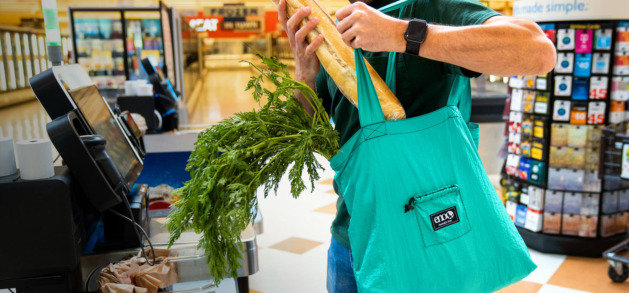 A person using an ENO Packable Tote as a reusable grocery bag in market environment. 