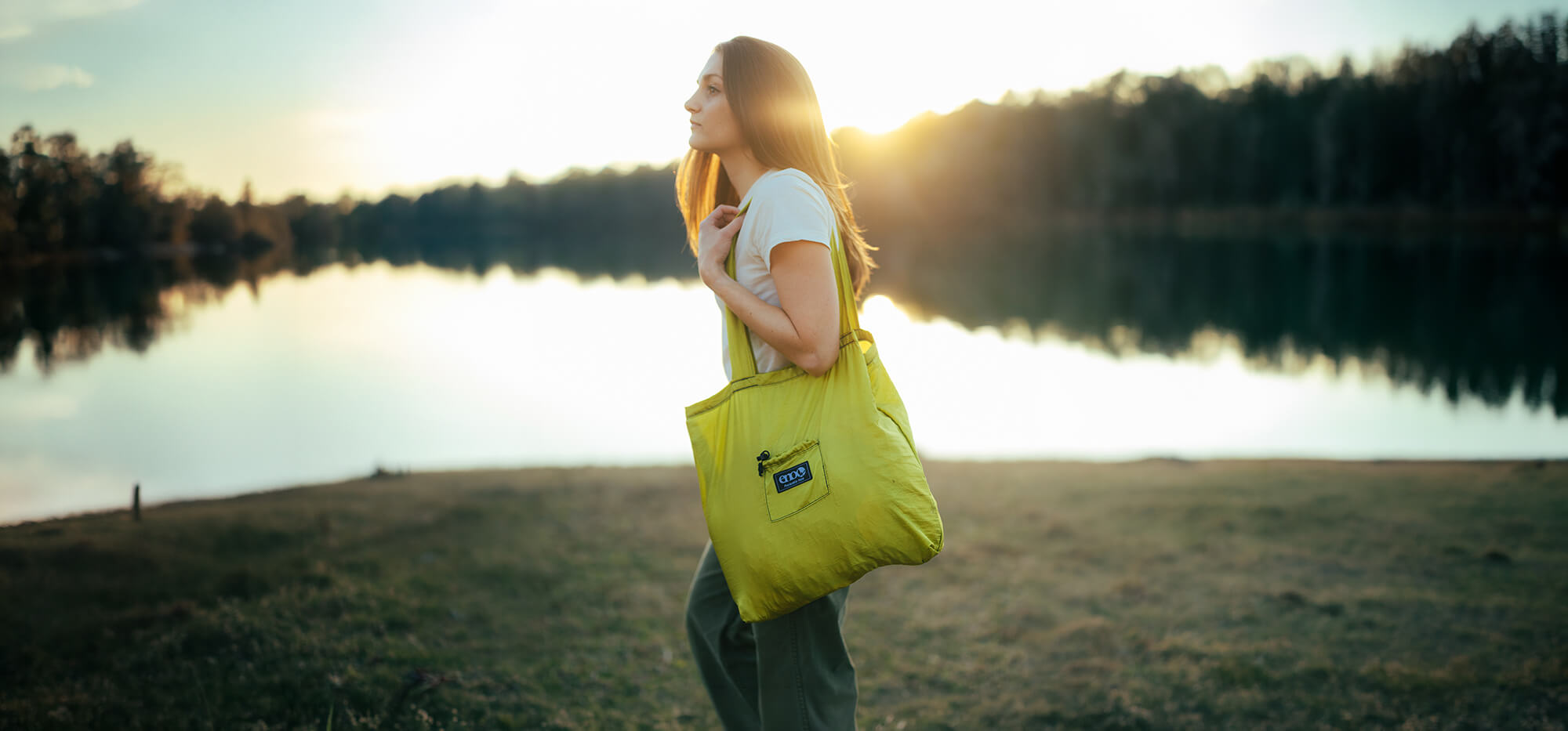 A person carrying a Packable Tote in Melon colorway in a lake setting.