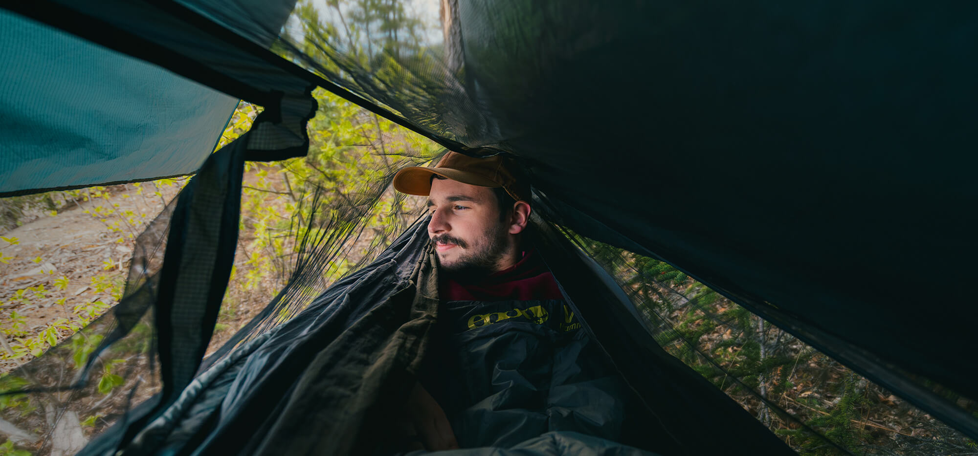 Man lying inside an ENO Hammock with an ENO Guardian Bug Net setup over it and a forest background