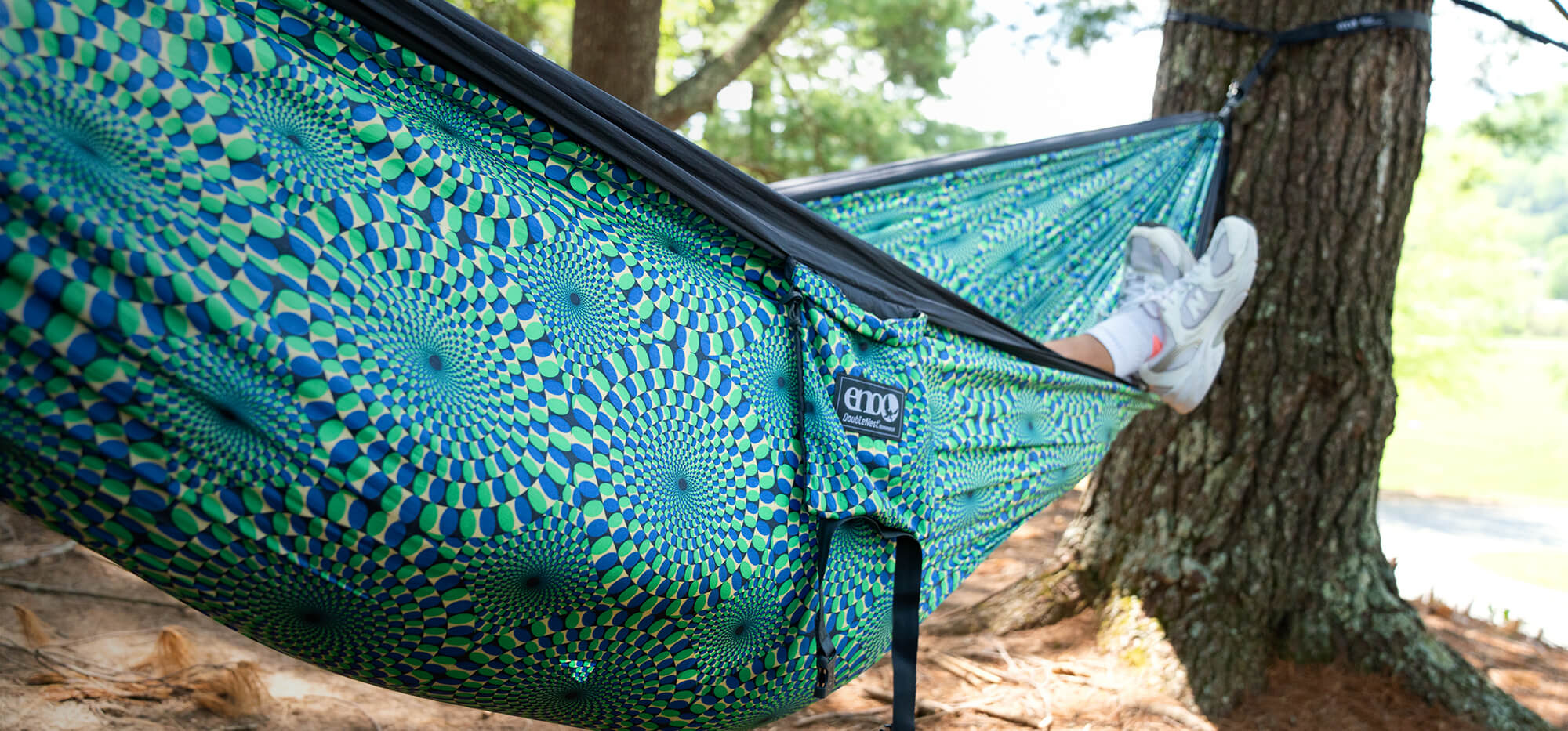 A person lays in an Optical Illusion ENO DoubleNest Hammock Print with their feet hanging out.