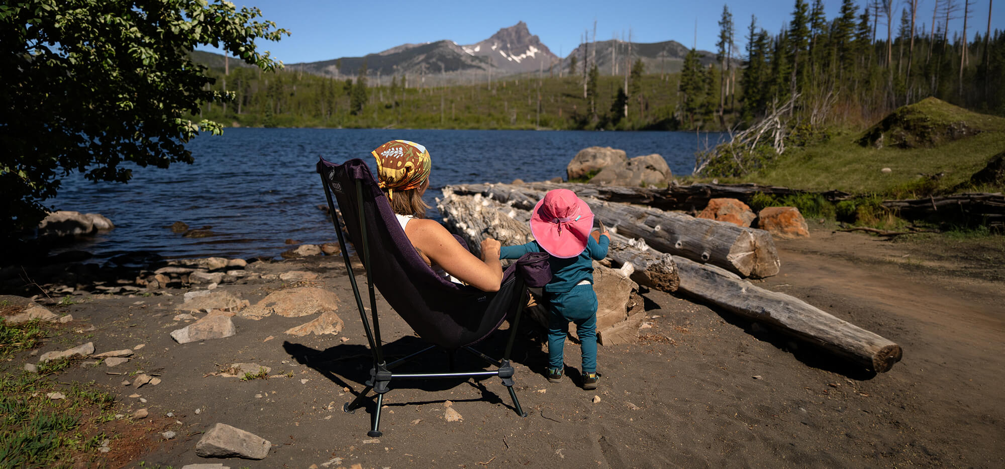 A person sitting lakeside in an ENO Lounger DL Chair with their child standing close by.