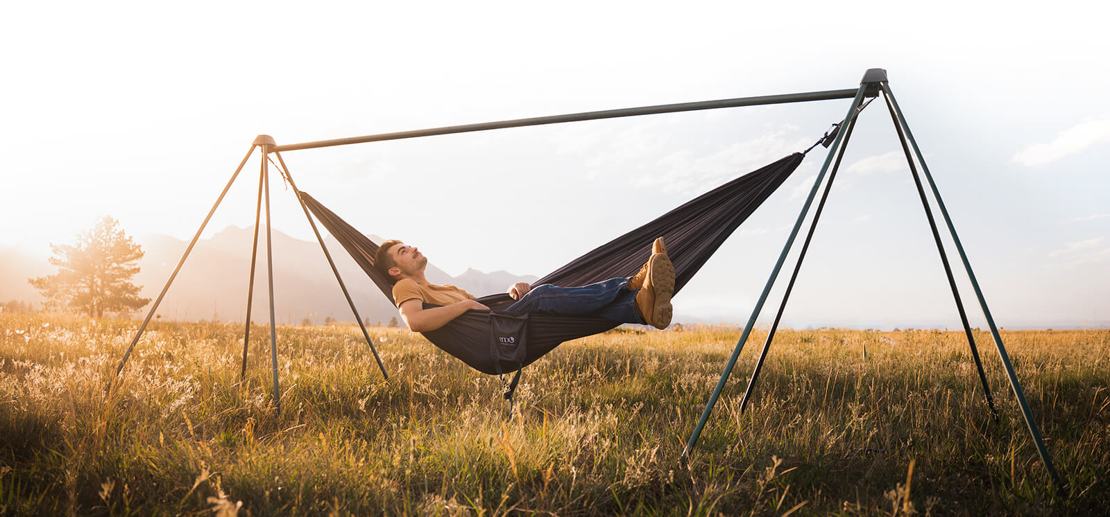Person relaxing in a hammock with a stand in a field during sunset