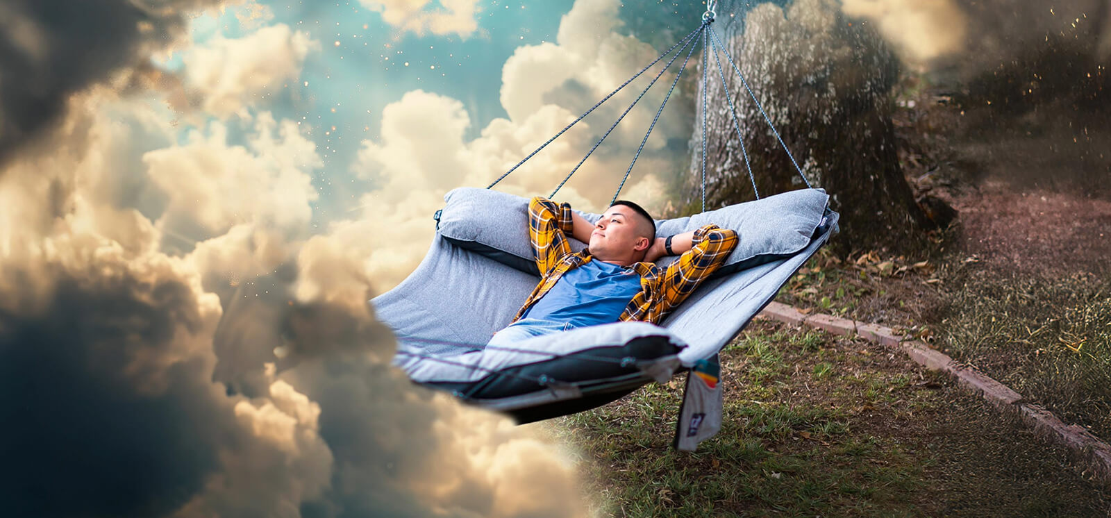 A young man lays with his hands behind is head in a ENO SuperNest Hammock while looking out into a void as the environment transforms into a vast blue sky with lofty clouds.