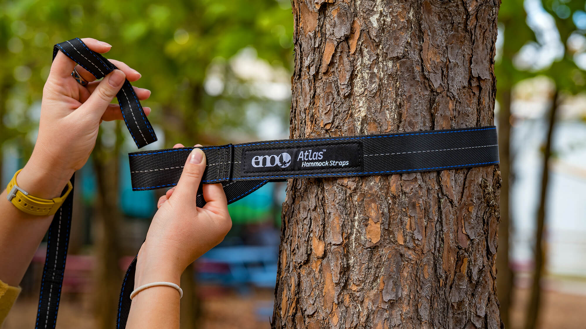 A close up image of a person wrapping ENO Atlas Hammock Straps around a tree and inserting the No-Knots-Needed adjustment strap through the strap end.