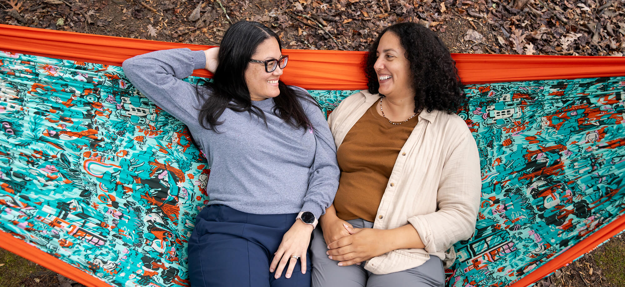 Two women sitting in an ENO Giving Back Hammock smiling while they look at each other.