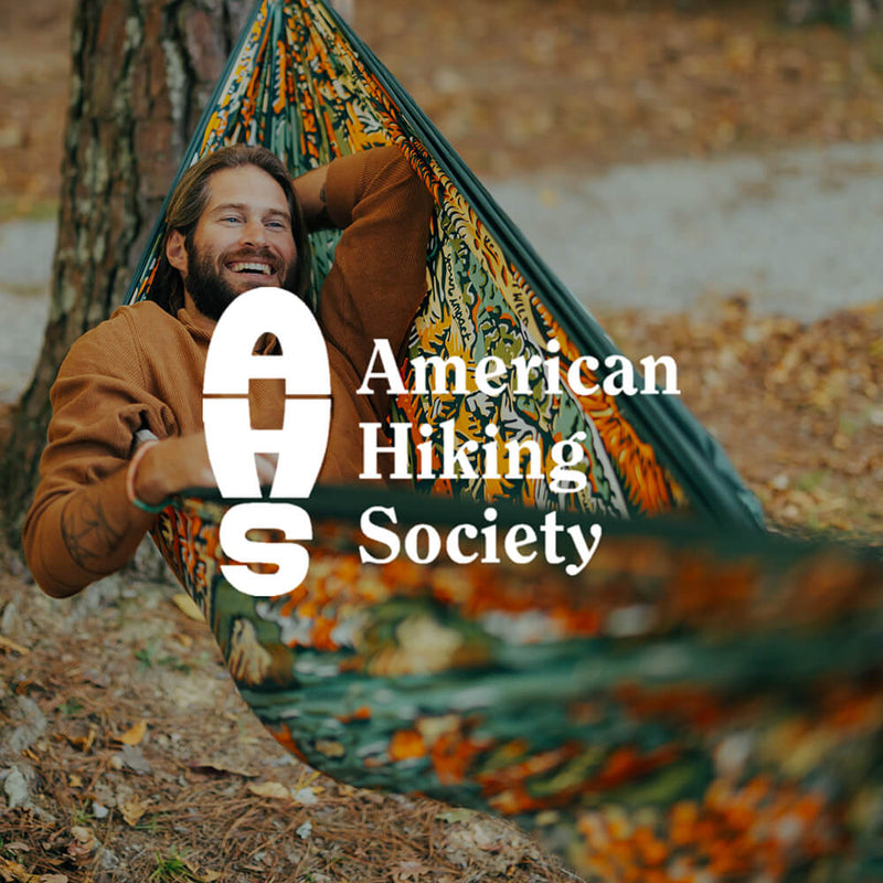 Person relaxing in the ENO Giving Back Hammock with the American Hiking Society logo overlay