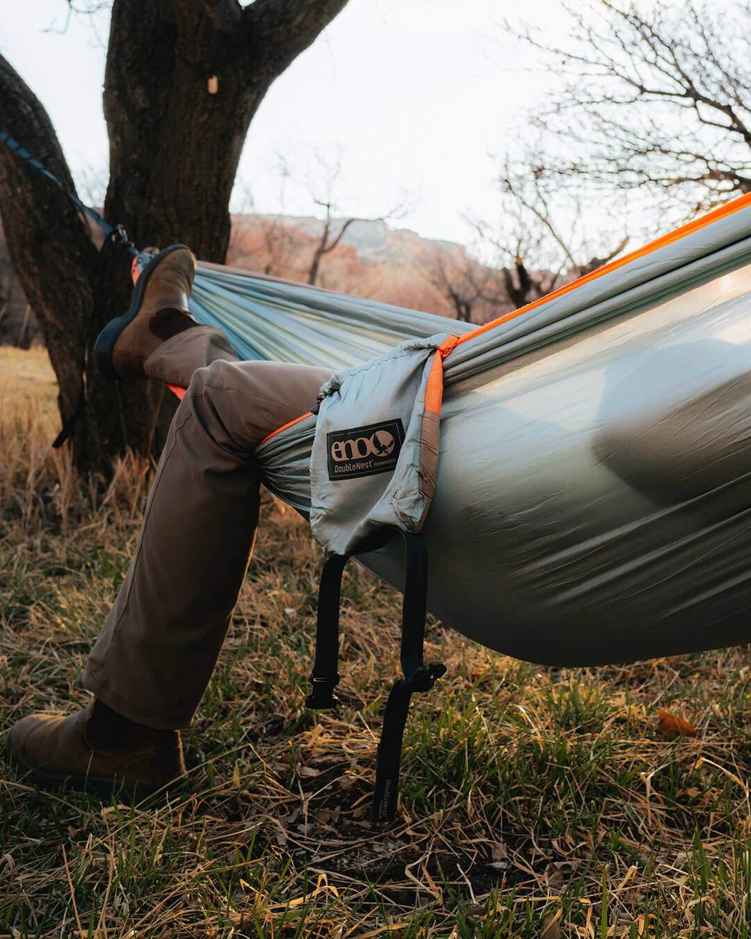 A person reclining in the Coastal Cocktail DoubleNest Hammock strung between two trees outdoors on grassy ground, with the brand patch 'endorphins' visible on the side.