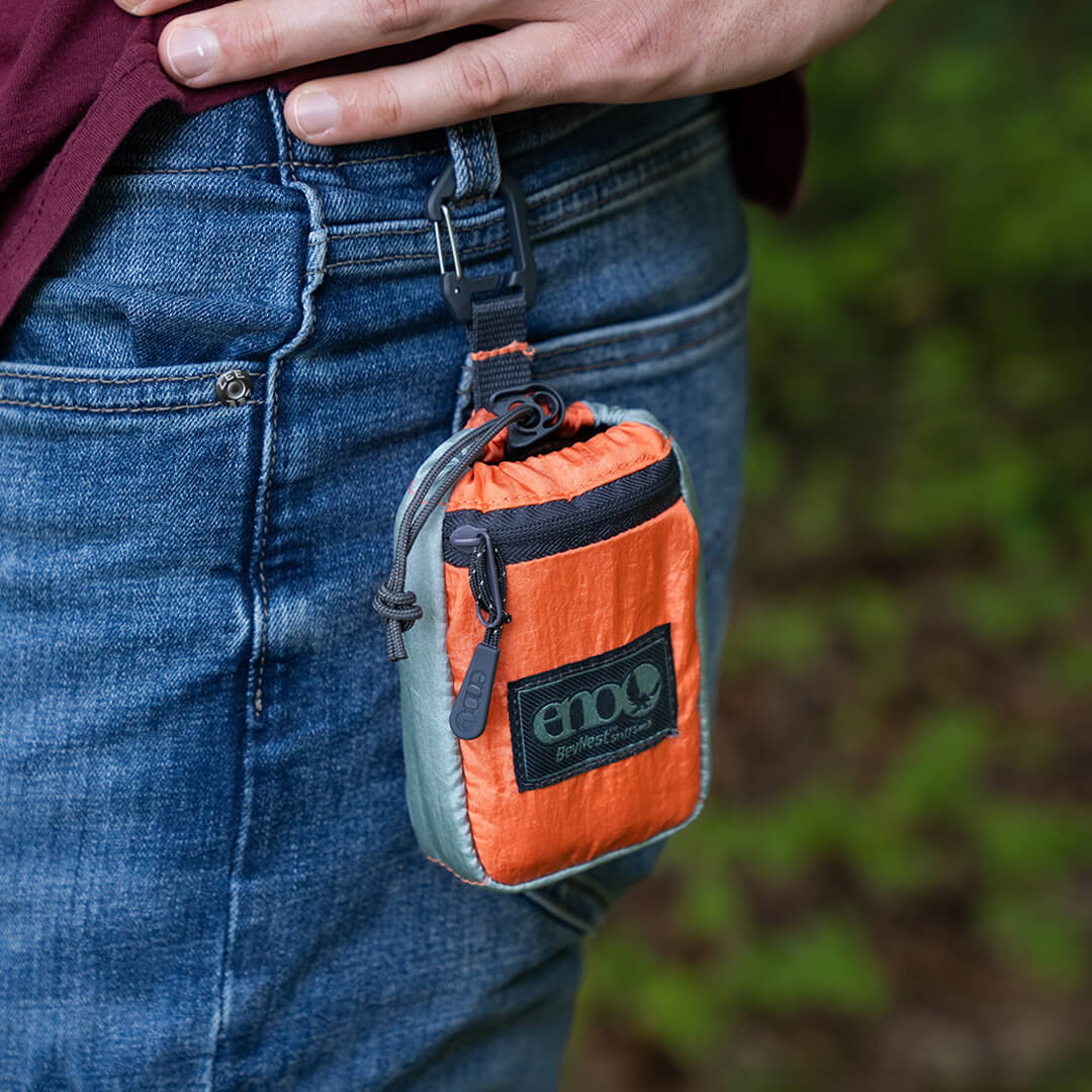 ENO BevNest Stuff Sack clipped onto a persons pant belt buckle loop with cinch cord pulled tight to keep belongings secure.