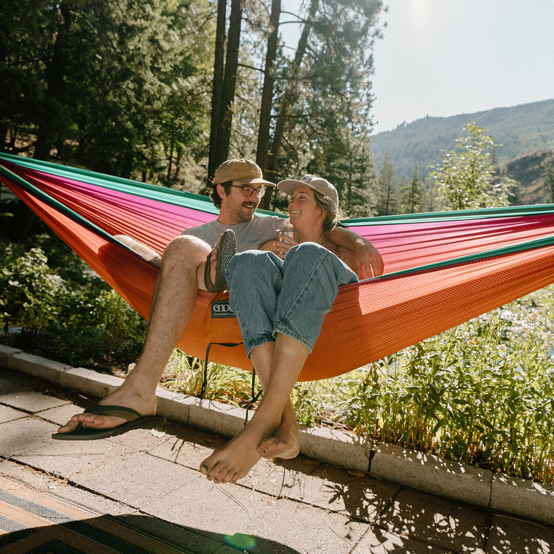 Couple sits in ENO DoubleNest Hammock Print hanging in front of forest.