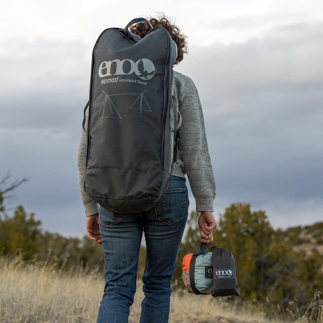 Person carrying packed up ENO Nomad Hammock Stand, DoubleNest Hammock, and Nomad Gear Loft in a trail setting.