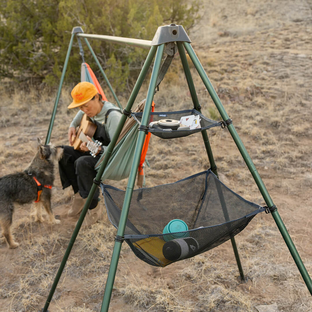 Gear packed into the Nomad Gear Loft shelf system, with a person sitting in a hammock with a dog and guitar in the background.