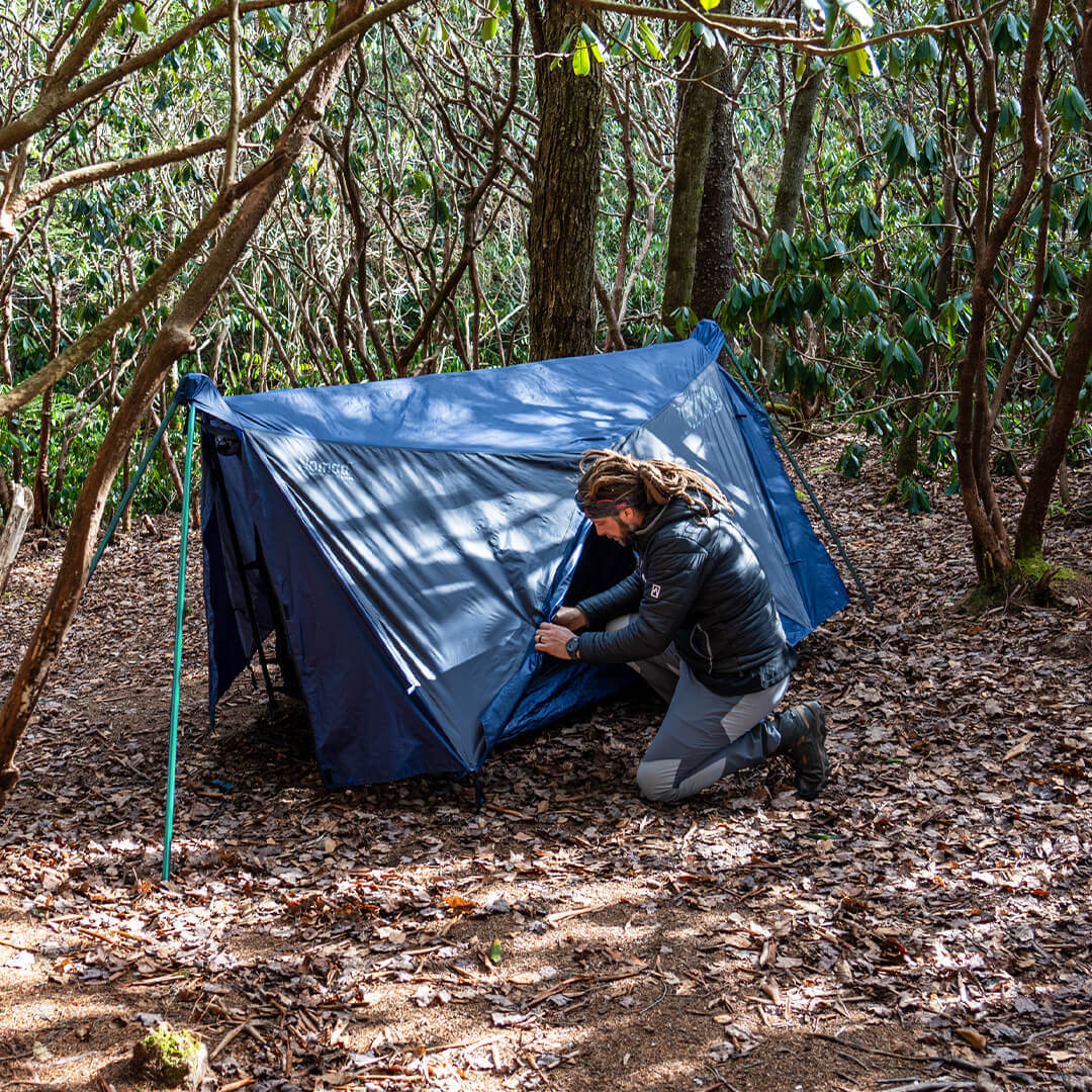 A man connects the ENO Nomad Shelter System to the Nomad Hammock Stand in lush forest.