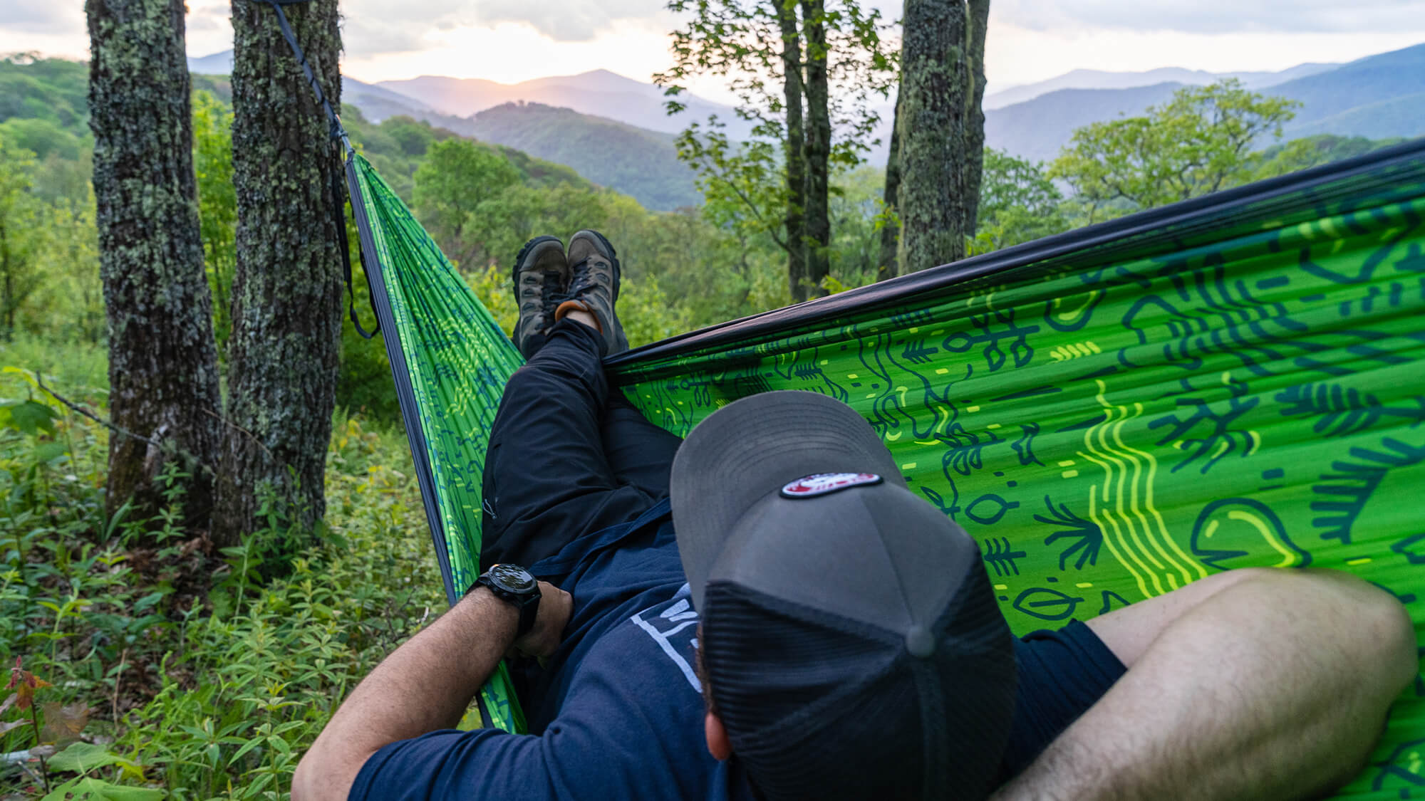 A person laying in an ENO portable hammock with their legs crossed while watching the sunset over the mountains. 