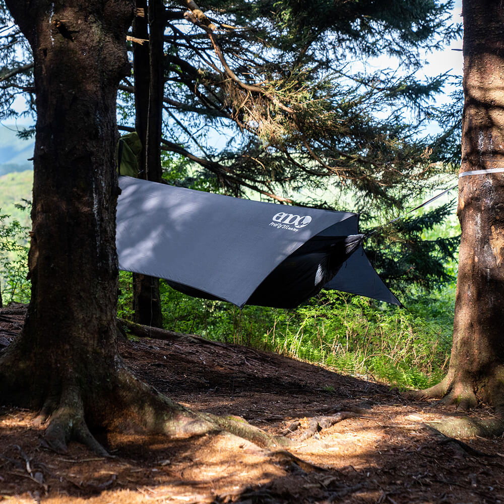 All-in-one ENO ultralight hammock tent consisting of hammock, hammock straps, bug net, and rain tarp set up between trees in woods. 