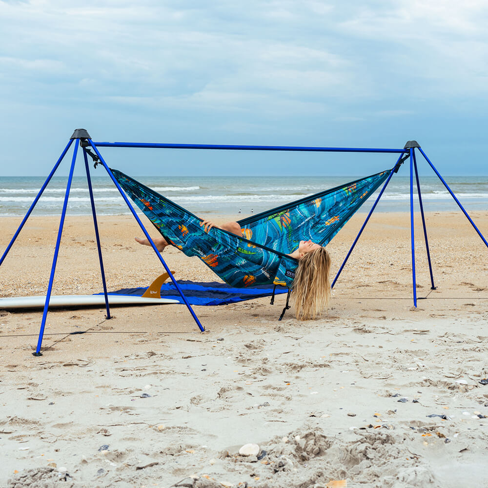 A woman leaning back on a sandy beach in an ENO hammock and beach hammock stand.