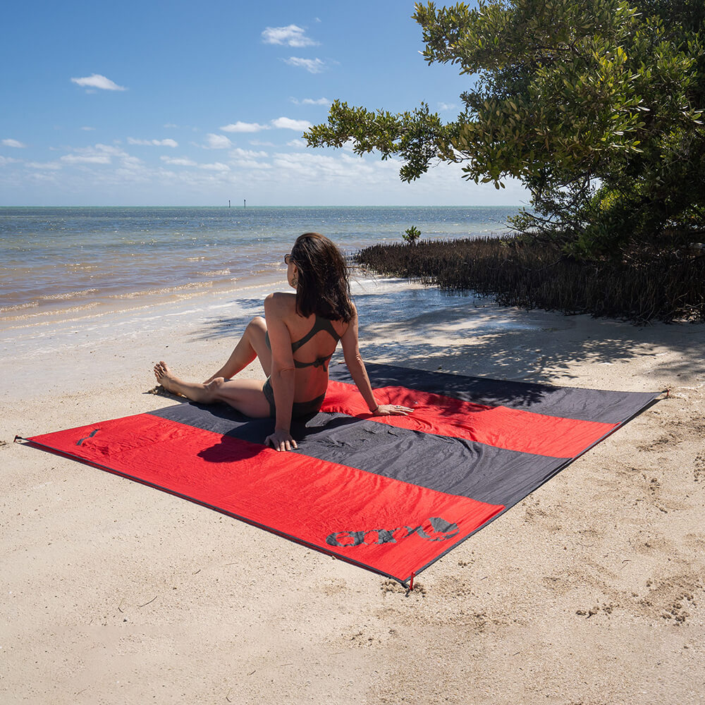 A woman in bathing suit on a beach looking onto the ocean on top of an ENO beach blanket.