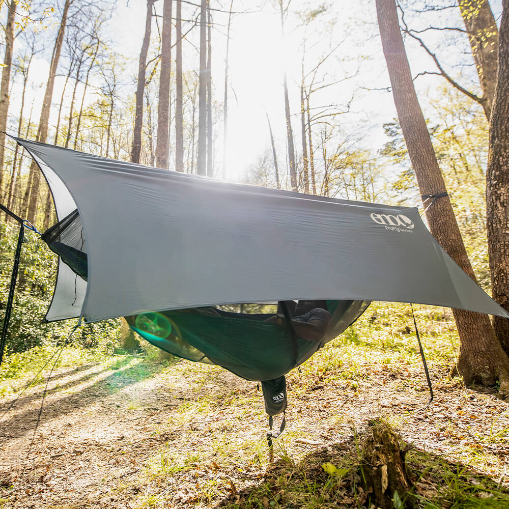 A person lying in an ENO hammock with hammock straps, a bug net, and a rain tarp between two trees.