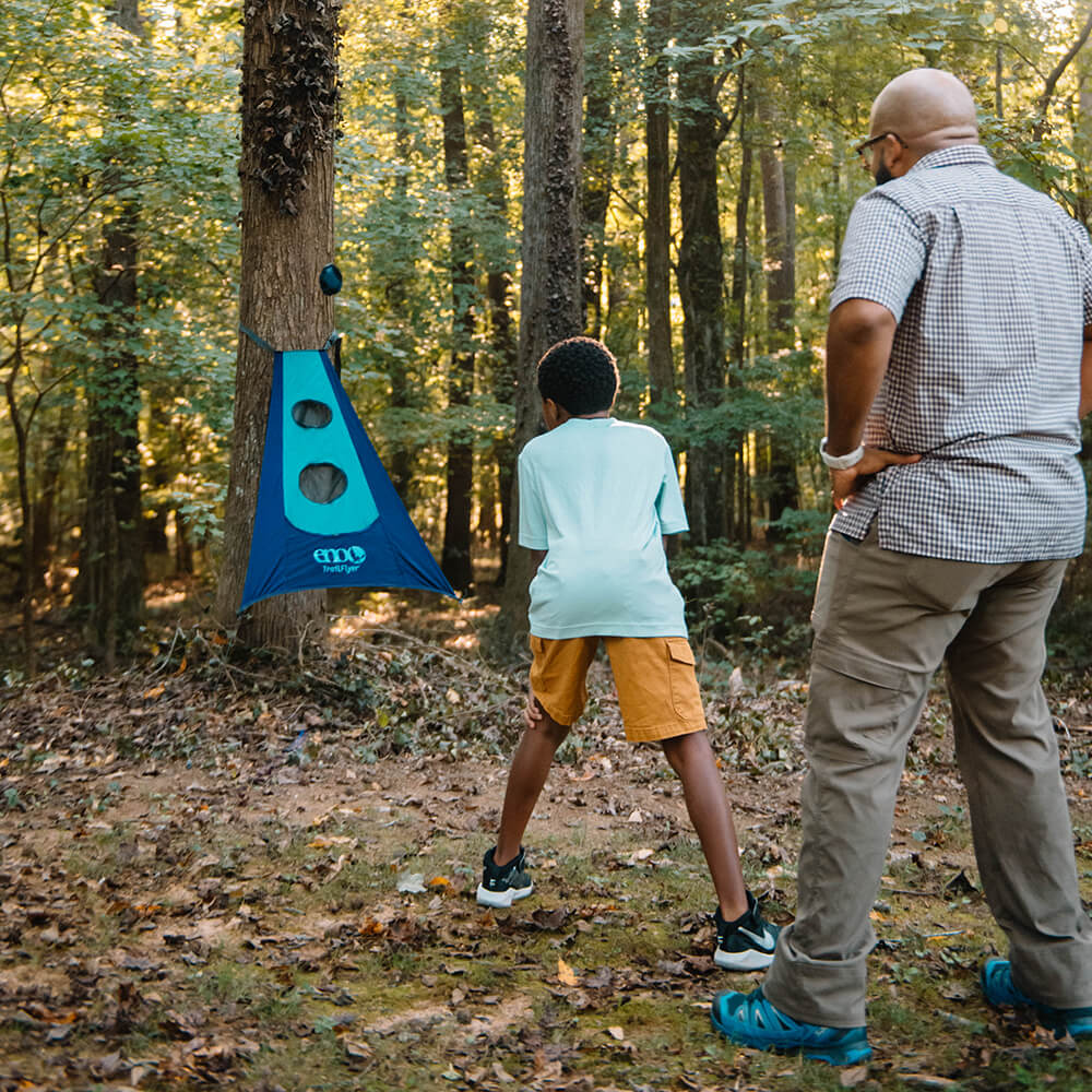 A child playing an ENO packable game in the woods while the father looks on.