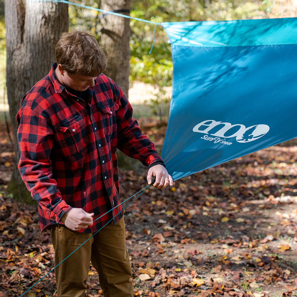 A man in a red flannel shirt adjusts his camping accessories to proper tension.