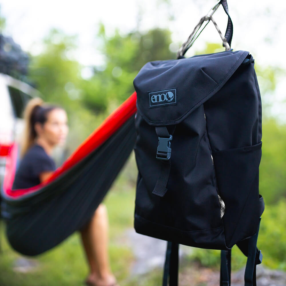 ENO pack hanging on a hammock as a woman sits in the hammock in the background. 