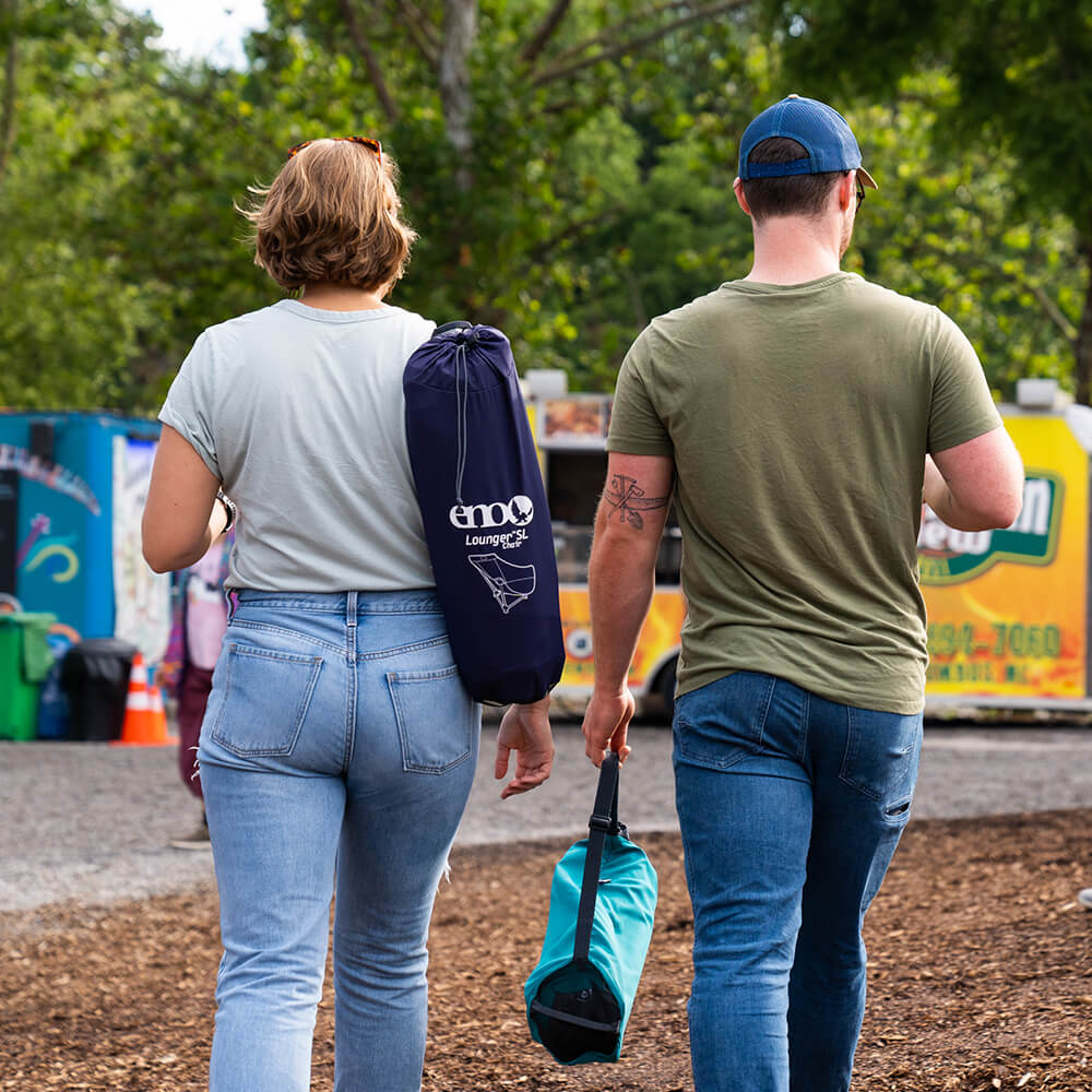 Couple in festival environment walking away from camera to set up ENO hammock lounge chairs. 