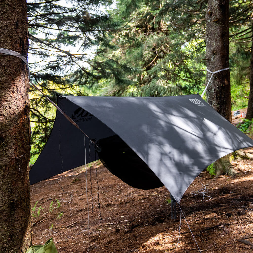 Three-quarter view of an ENO hammock system set up in the woods with ultralight hammock straps, bug net, rain tarp, and hammock.