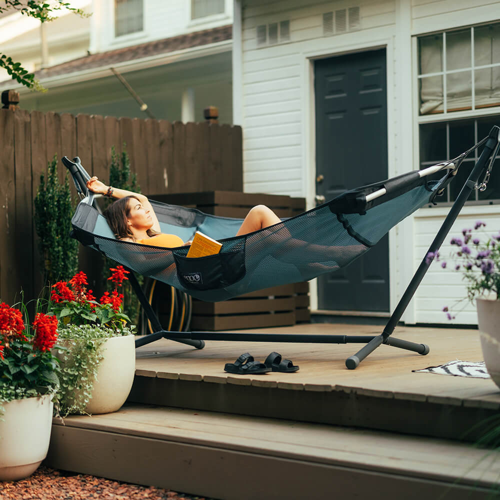 A young woman relaxing amongst flower pots on the back porch of a townhouse in an ENO backyard hammock and portable hammock stand.