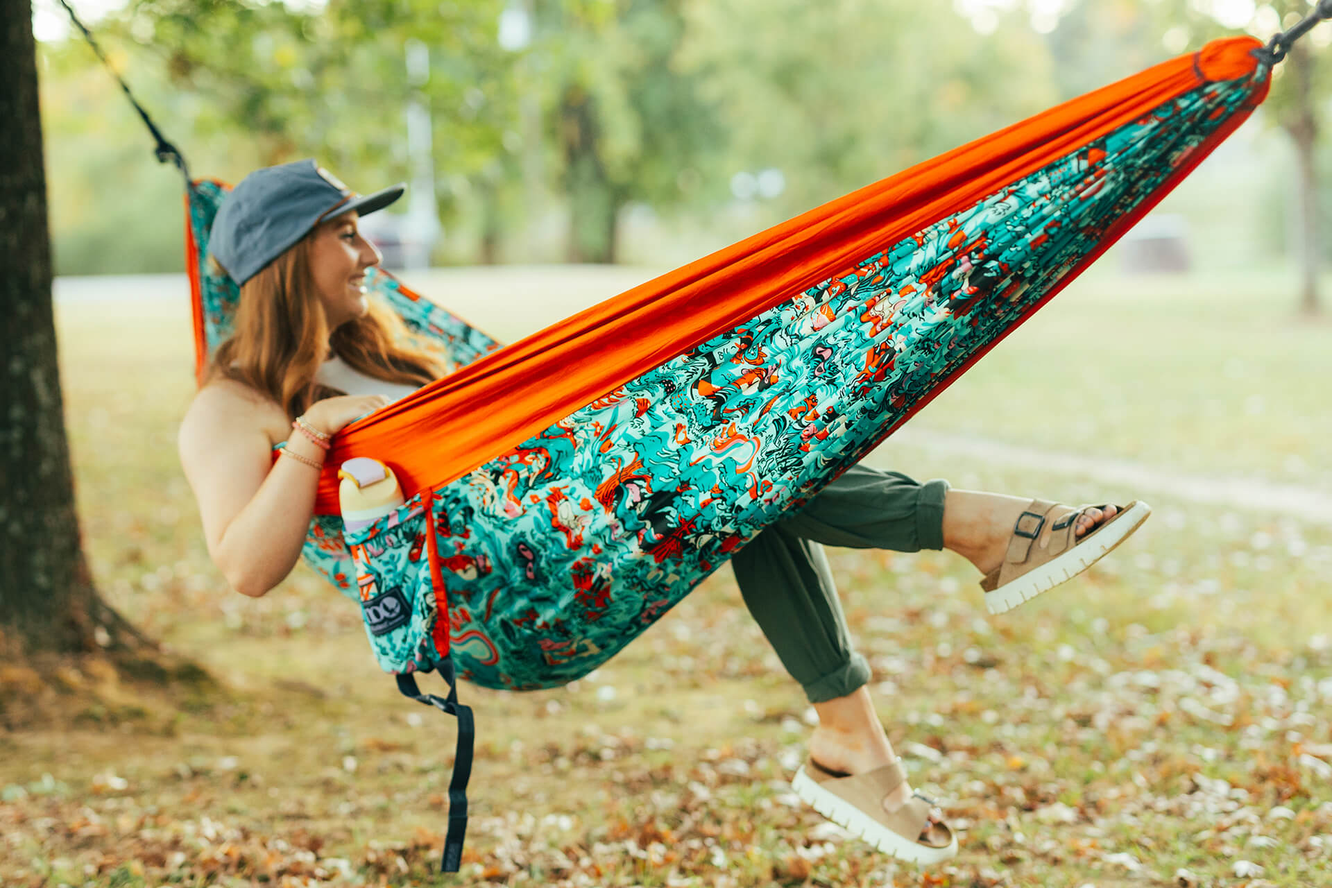 Person sitting in an ENO In Good Company Giving Back Hammock with a patterned design in an outdoor setting.