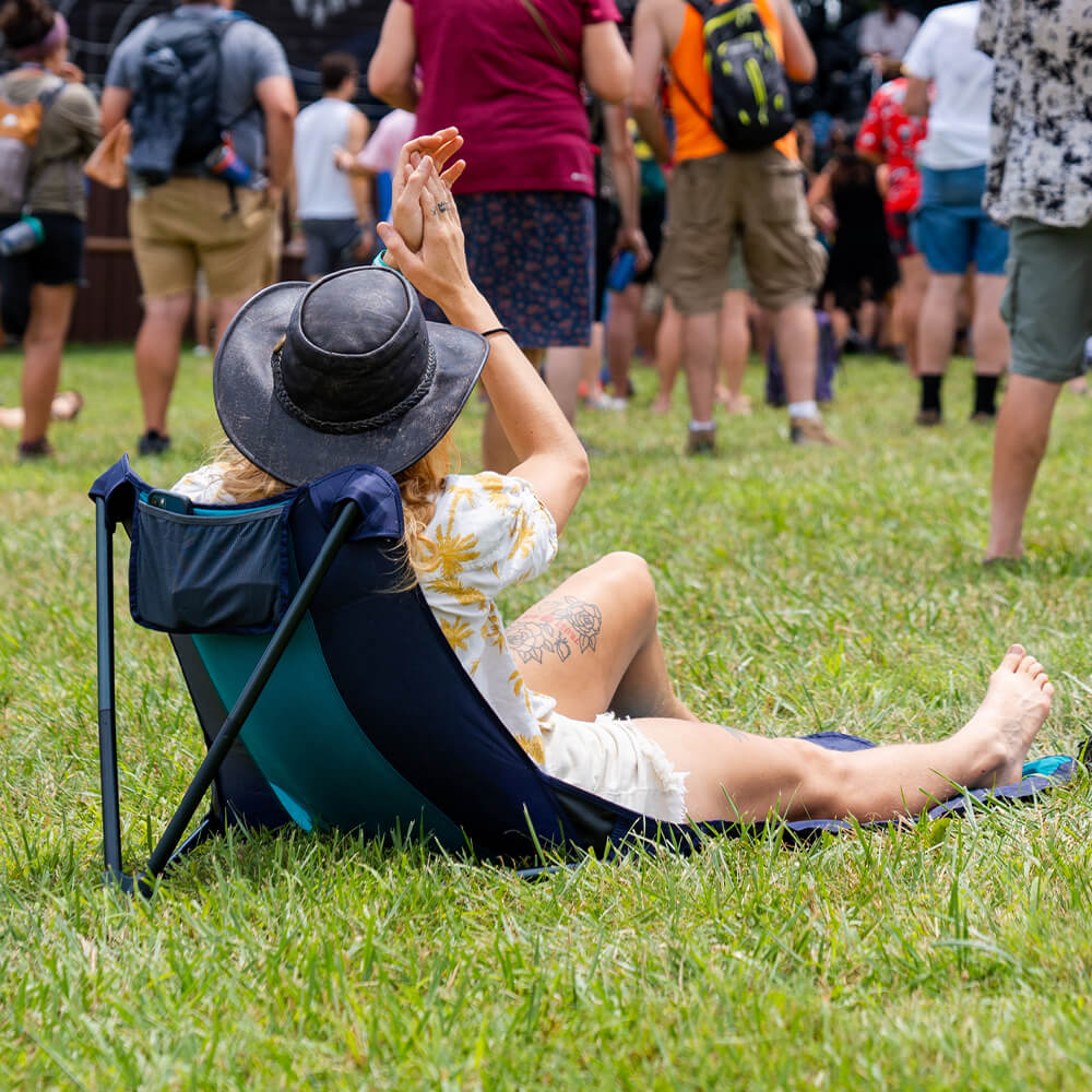 A woman in a hat cheers on a festival performance on an ENO packable ground chair.