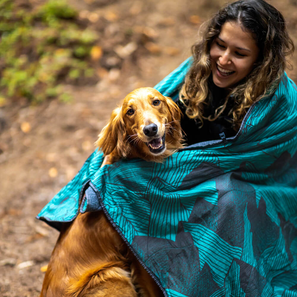 A woman smiles as she pets her dog in an ENO camp quilt.